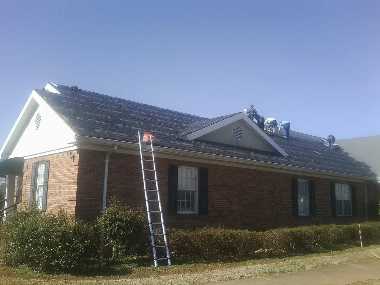 Crew tearing shingles off a brick ranch roof with a ladder set — Emergency Roof Repair work by our crew in Garrett Park