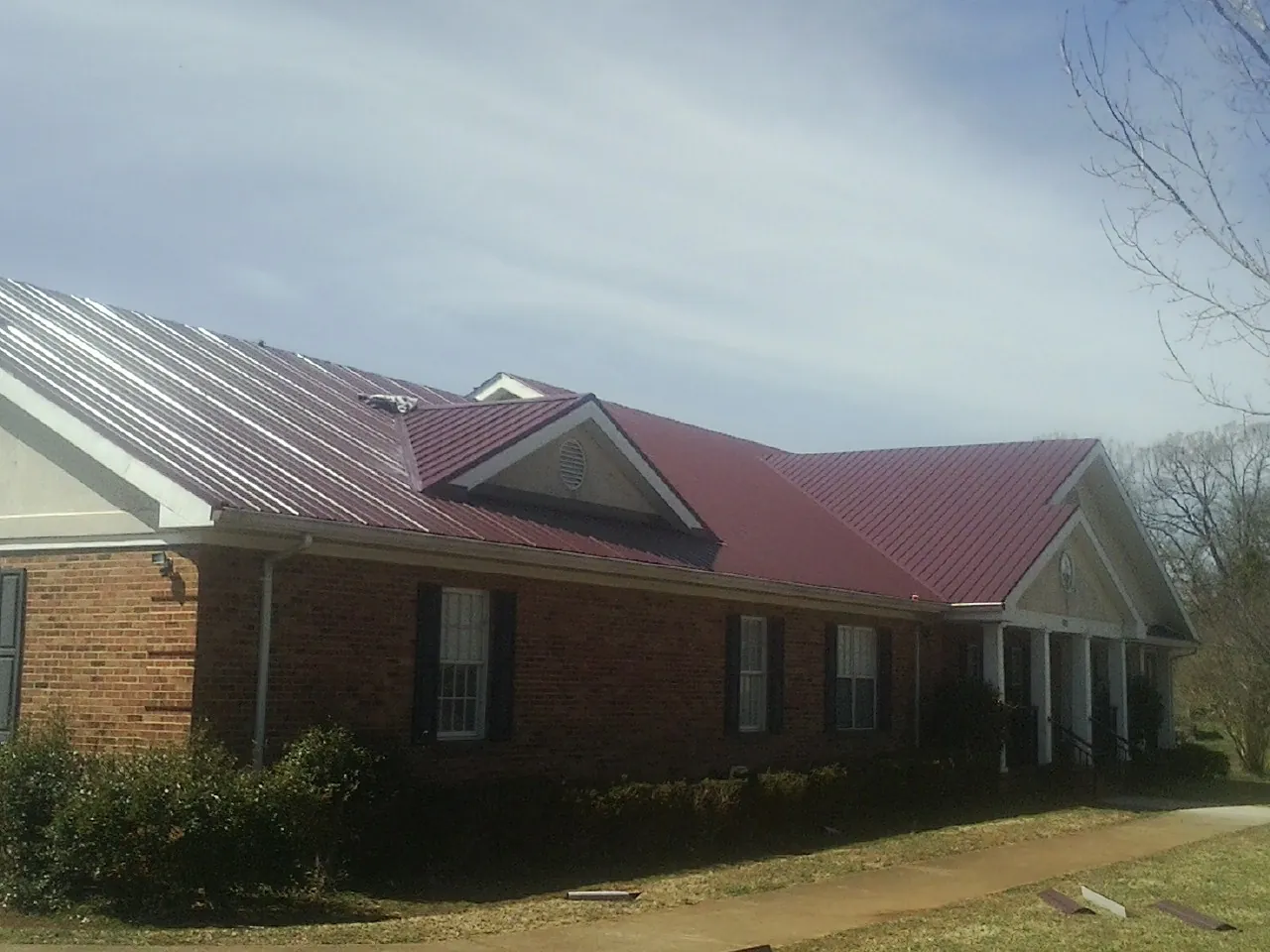 Red metal roof with gabled entries on a long brick building, from a Hail Damage Roof Repair job in Garrett Park