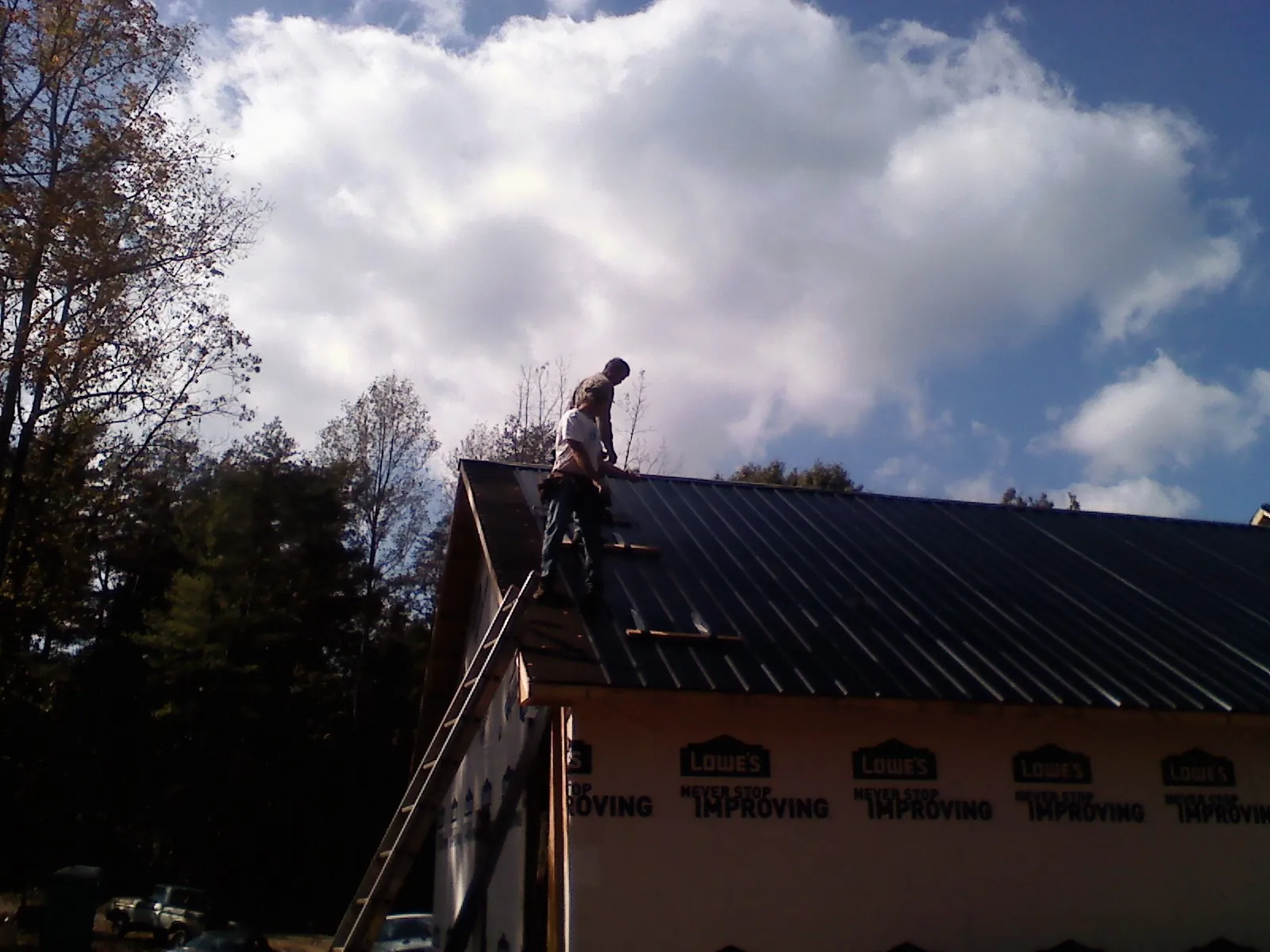 Roofer fastening dark metal panels high against a cloudy sky, from a Roof Inspection job in Garrett Park