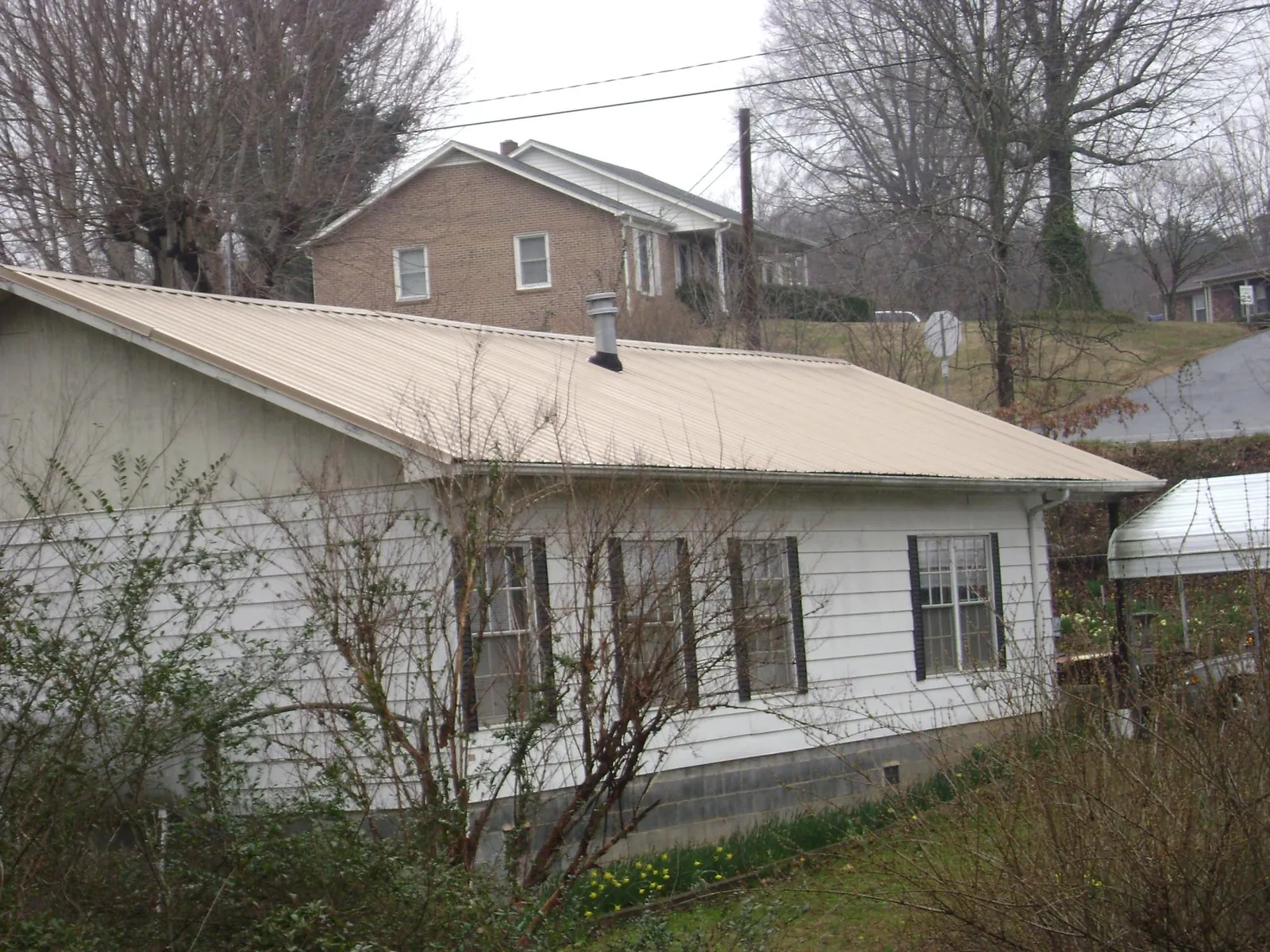 Tan metal roof on a white sided house set into a hillside — Commercial Roofing by Roofing Brothers in Garrett Park